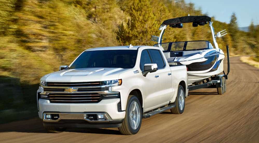 A white 2020 Chevy Silverado 1500, which wins when comparing the 2020 Chevy Silverado 1500 vs 2020 Toyota Tundra, is towing a large boat on a dirt road.
