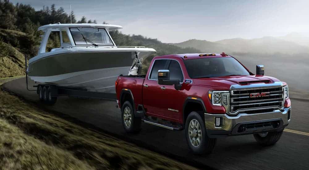 A red 2020 GMC Sierra 2500HD is towing a large boat up a tree lined hill.
