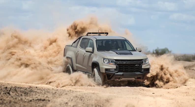 A tan 2021 Chevy Colorado ZR2, which is a popular option among lifted trucks, is drifting in the desert with a dust cloud forming behind it.