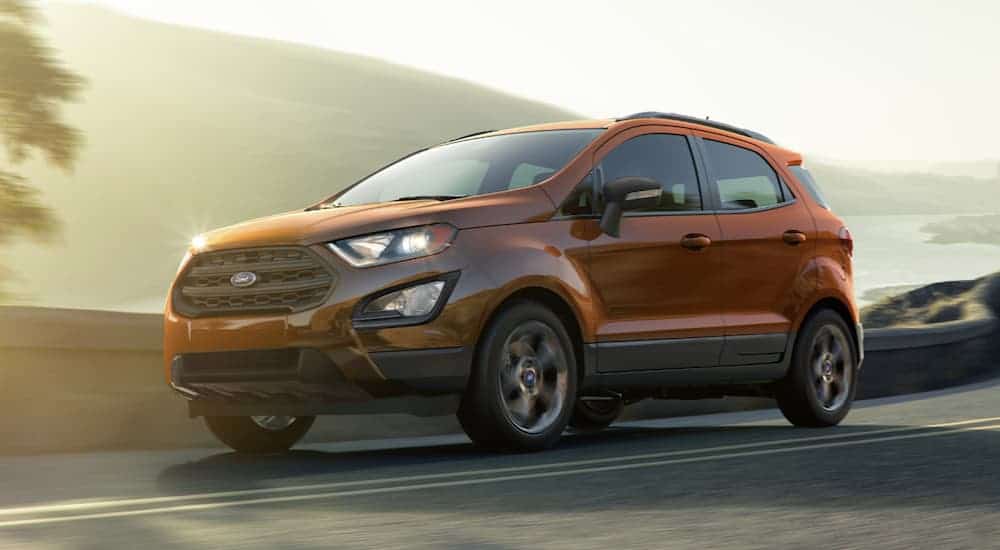 An orange 2020 Ford Ecosport is driving next to a lake on a sunny day.
