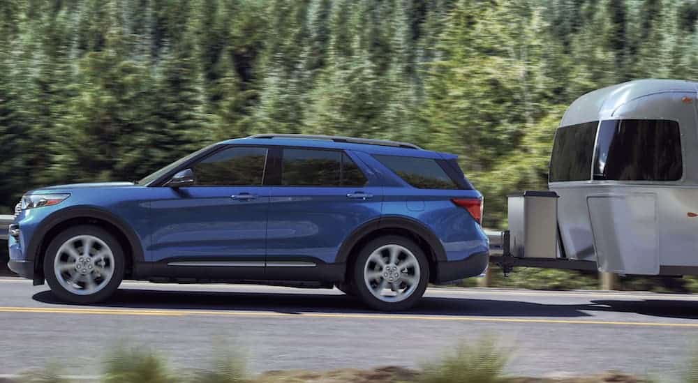 A blue 2020 Ford Explorer, which is one of the most popular options among Ford SUVs, is towing a large Airstream on a tree lined road.
