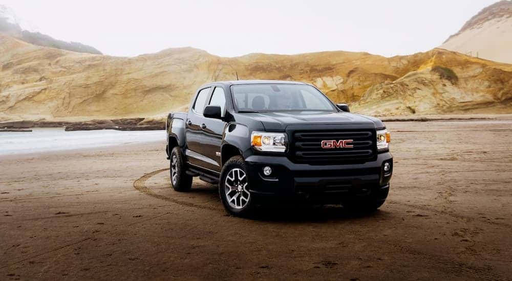 A black 2020 GMC Canyon, the smallest of the GMC trucks, is parked on the sand at a beach.
