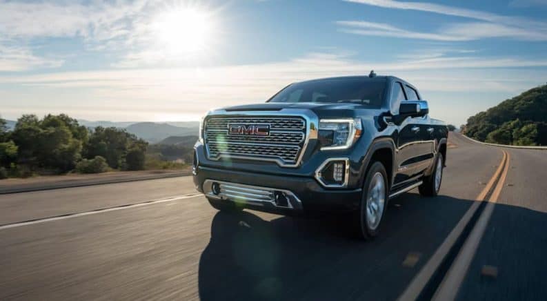 A dark grey 2020 GMC Sierra 1500 Denali is driving on a sunny highway with mountains in the distance.