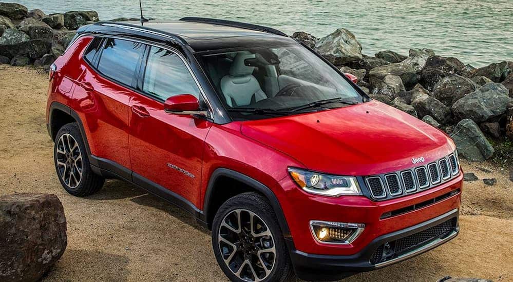 A red 2020 Jeep Compass is parked a rocky shore line at a beach. 