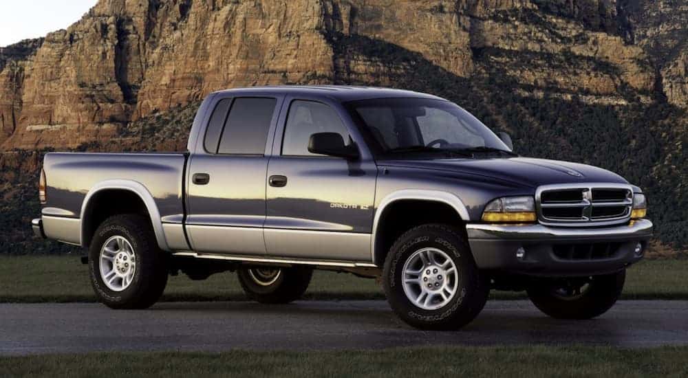 A blue 2003 Dodge Dakota is parked in front a large rock hill.