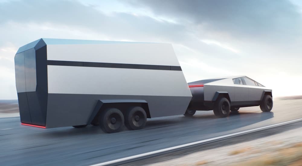 A Tesla Cybertruck is towing a trailer up hill.