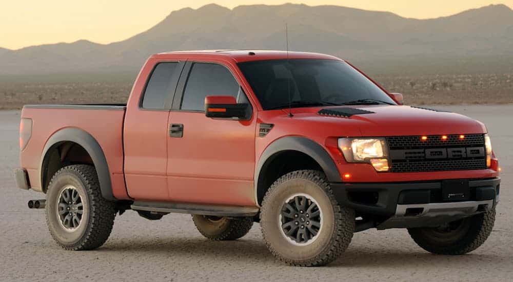 A red 2010 Ford Raptor, which is a popular option among used Ford trucks, is parked in the desert with mountains in the distance. 