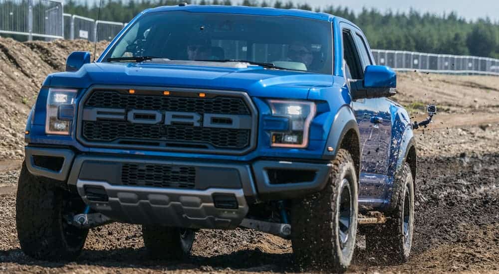 A blue 2017 Ford Raptor, which is a popular option among used Ford trucks, is driving through a mud pit. 