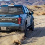 A blue 2019 Ford Raptor is shown from the rear while driving on a dirt road.