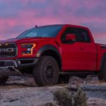A red 2019 Ford Raptor is parked on a dirt hill with a colorful sunset behind it.