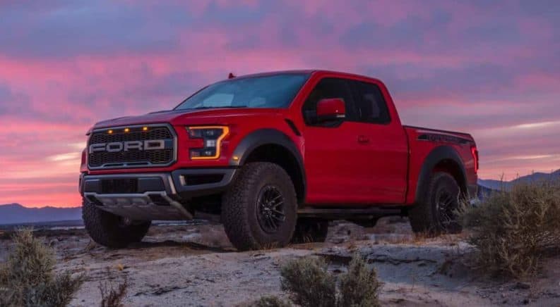 A red 2019 Ford Raptor is parked on a dirt hill with a colorful sunset behind it.