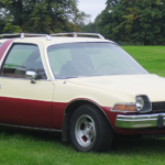 A red and white 1978 AMC Pacer, one of the worst condition vehicles in history, is in a field.
