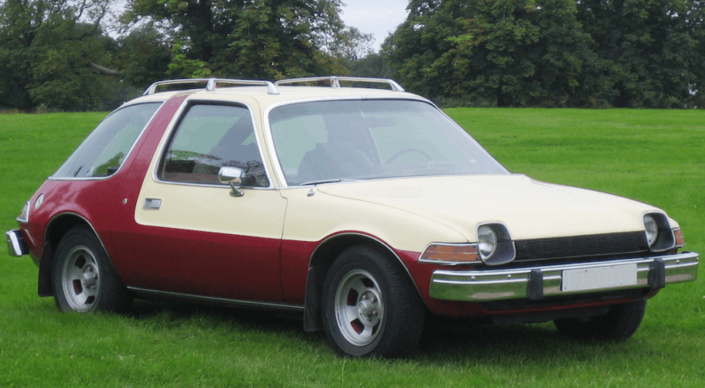 A red and white 1978 AMC Pacer, one of the worst condition vehicles in history, is in a field.