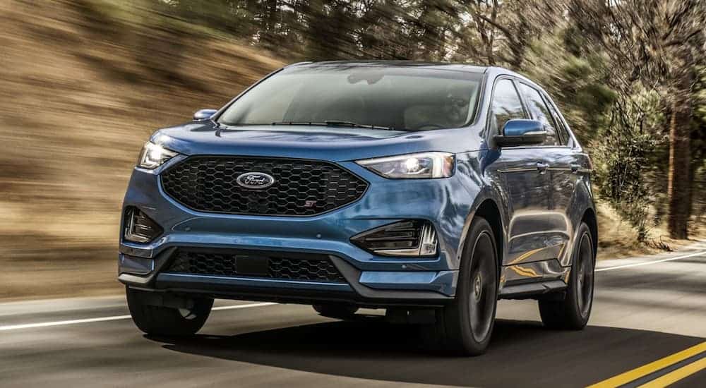 The front of a blue 2020 Ford Edge is shown while driving on a tree-lined road.