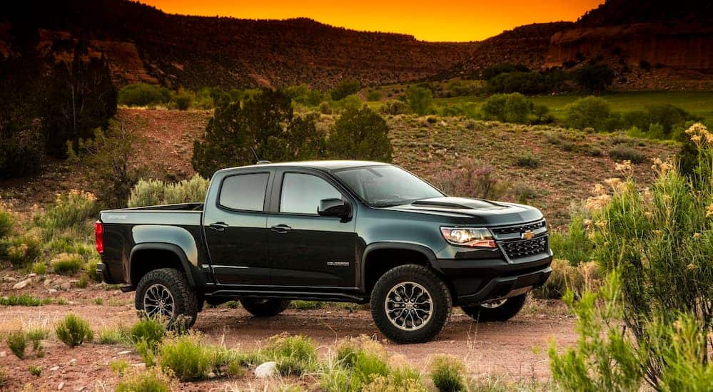 A black 2020 Chevy Colorado, which wins when comparing the 2020 Chevy Colorado vs 2020 Toyota Tacoma, is parked on a dirt path with mountains in the distance. 