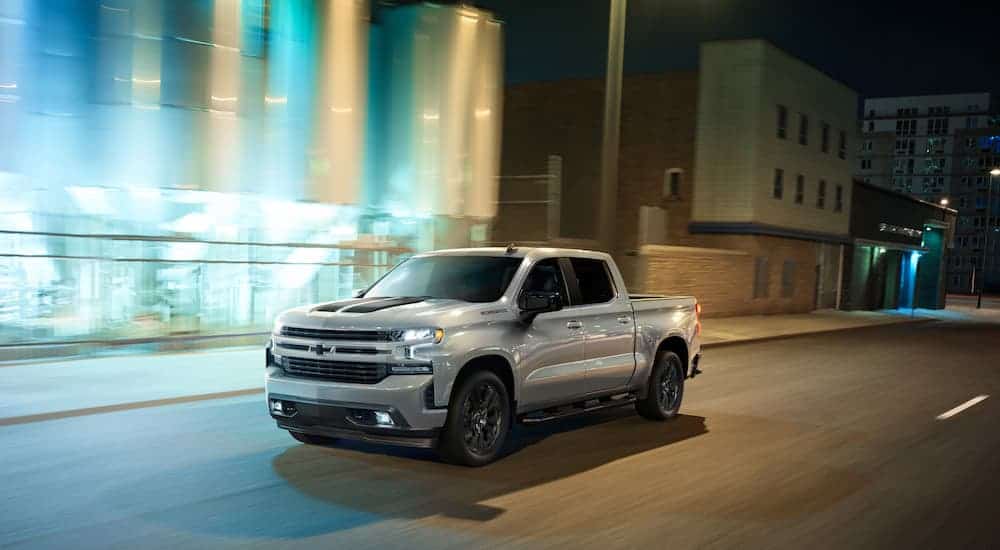 A silver 2020 Chevy Silverado 1500 Rally Edition is driving on a city street at night.
