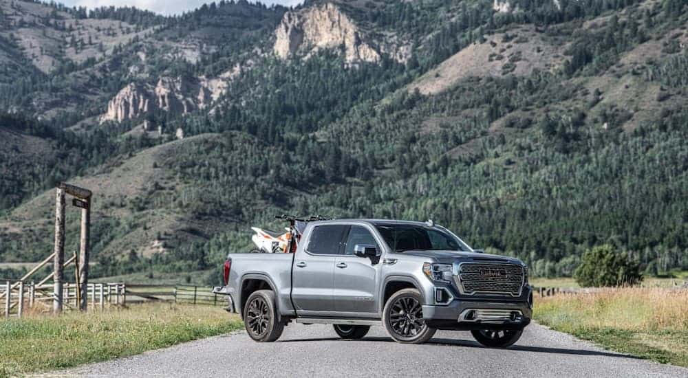A grey 2020 GMC Sierra is parked in front of a mountain with dirt bikes in the bed.