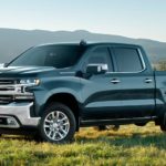 A dark grey 2020 Chevy Silverado 1500, which wins when comparing the 2020 Chevy Silverado vs GMC Sierra 1500, is parked on grass in front of mountains.