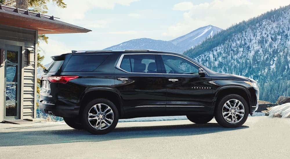 A black 2020 Chevy Traverse is parked in front of a house while facing snow covered mountains. 
