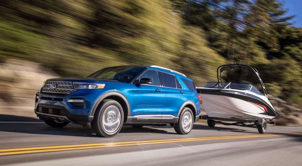 A blue 2020 Ford Explorer is towing a boat on a treelined road. 