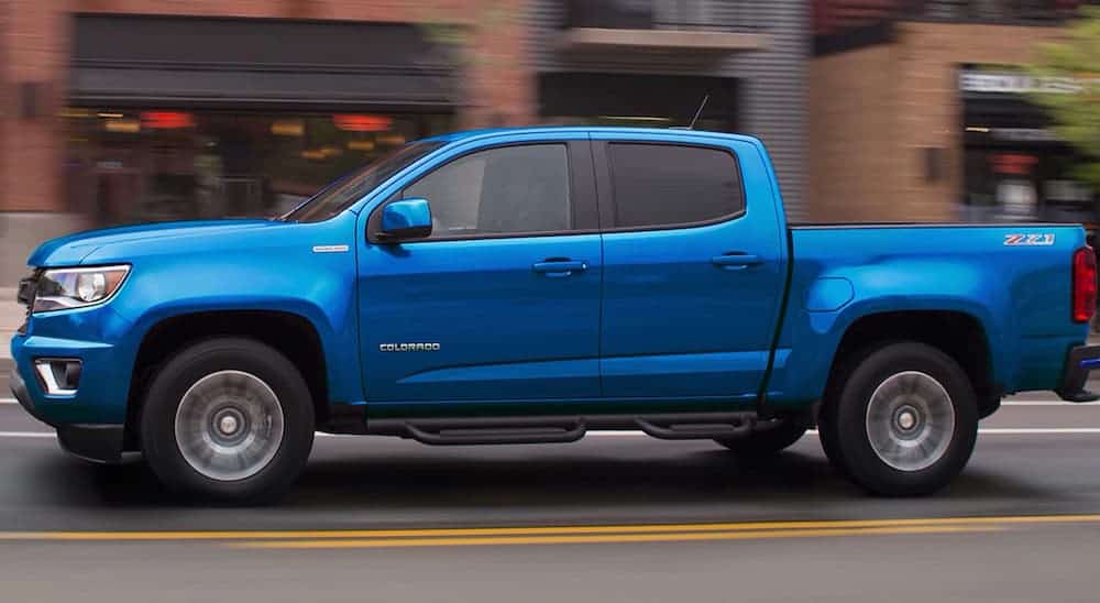 A blue 2020 Chevy Colorado is shown from the side while driving past blurred buildings. 