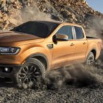 A golden 2020 Ford Ranger, which win when comparing the 2020 Ford Ranger vs 2020 Chevy Colorado, is driving on a dirt path next to a rock wall.