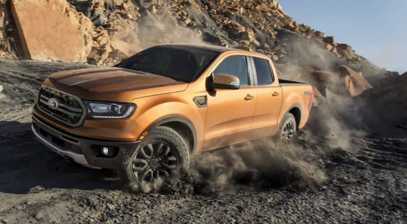 A golden 2020 Ford Ranger, which win when comparing the 2020 Ford Ranger vs 2020 Chevy Colorado, is driving on a dirt path next to a rock wall.
