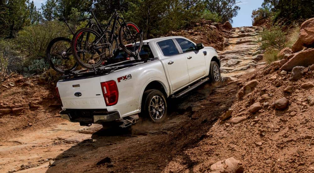 A white 2020 Ford Ranger, which wins when comparing the 2020 Ford Ranger vs 2020 Jeep Gladiator, is off-roading uphill with bikes in the bed.
