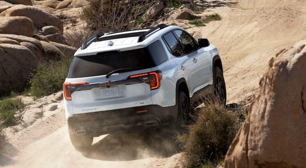 A white 2020 GMC Acadia AT4, which wins when comparing the 2020 GMC Acadia vs 2020 Jeep Grand Cherokee, is driving up a dirt hill. 
