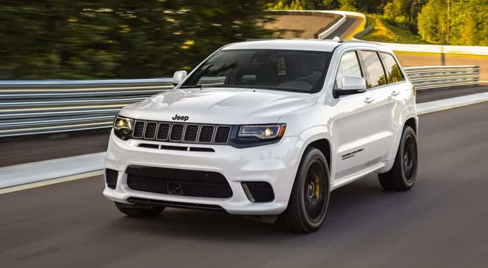 A white 2020 Jeep Grand Cherokee Trackhawk is driving on a treelined racetrack. 