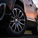 A low angle closeup of a black 2020 GMC Acadia Denali tire with the body reflecting a vibrant sunset.