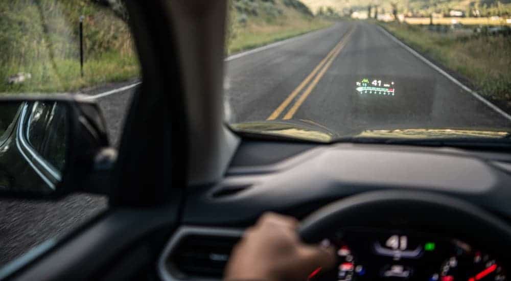 Hands on a steering-wheel are driving on a highway using the Heads up system of a 2020 GMC Acadia.