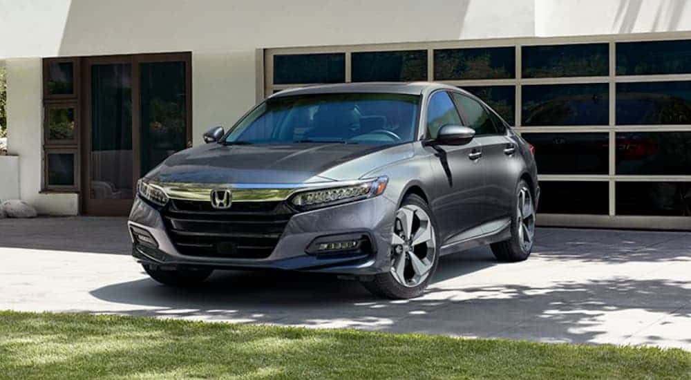 A grey 2020 Honda Accord Touring is parked in front a black garage door on a white house.