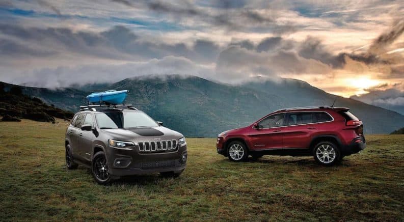 A dark grey 2020 Jeep Cherokee is parked next to a burgundy one in front of mountains.