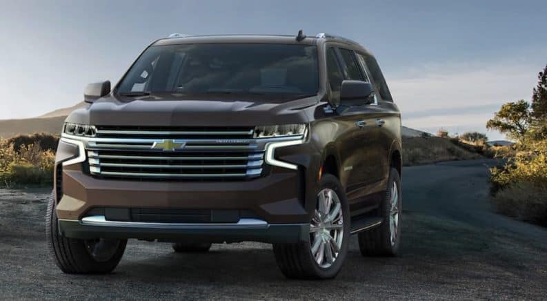 A brown 2021 Chevy Suburban is parked on a dirt path that's over looking trees.