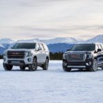 A white 2021 GMC Yukon AT4 and black 2021 GMC Yukon Denali are parked on a snowy field.