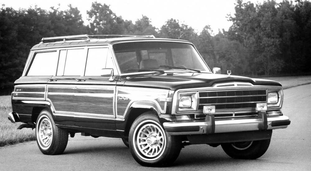 A black and white photo of a 1970 Jeep Grand Wagoneer that is parked on a street.