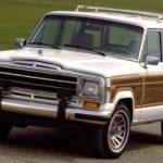 A white and wood-paneled 1987 Jeep Grand Wagoneer is parked on a road, this is the inspiration for the 2021 Jeep Grand Wagoneer.