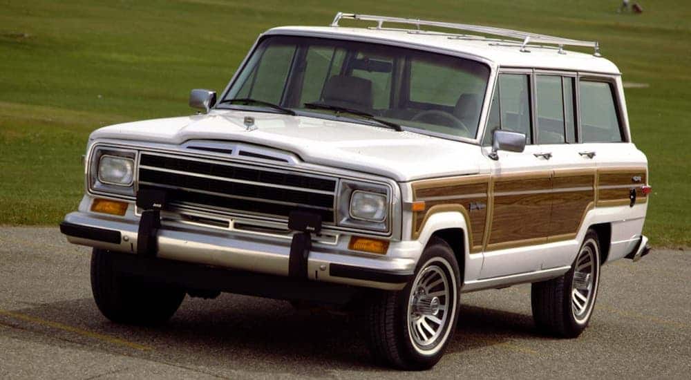 A white and wood-paneled 1987 Jeep Grand Wagoneer is shown parked on a road.