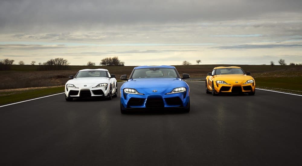 Three 2021 Toyota Supras, one white, one blue, one yellow, are driving on a racetrack.