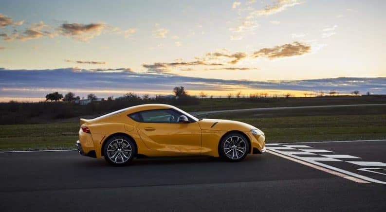 In current auto news, the 2021 Toyota Supra is taking off, shown here a yellow Supra is at the finish line of a racetrack.