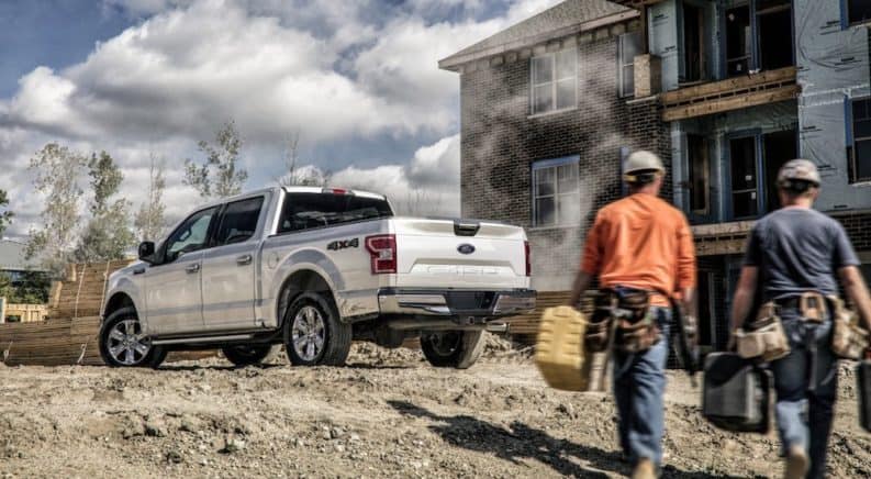 Two construction workers are walking towards a silver Ford F-150 on a job site.