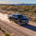 A black 2019 Ram 1500 is driving on a dirt road in the desert.