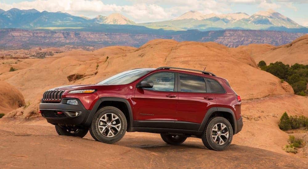 A red 2017 Jeep Cherokee Trailhawk is climbing over rocks on a desert mountain.