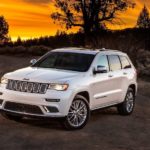 A popular used car, a white 2017 Jeep Grand Cherokee, is parked on the side of a road in front of a vibrant sunset.
