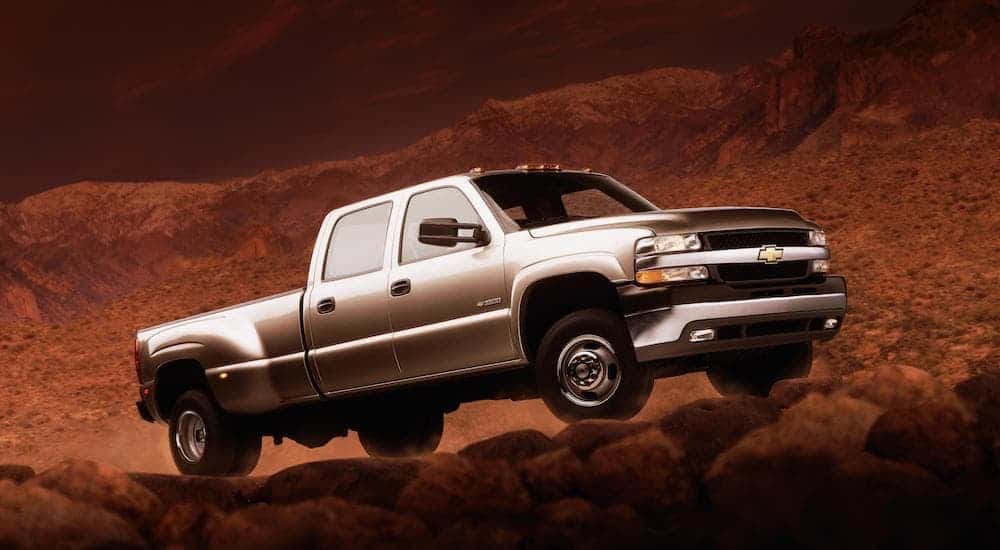 A silver 2001 Chevy Silverado HD is driving up a dirt hill at dusk. 