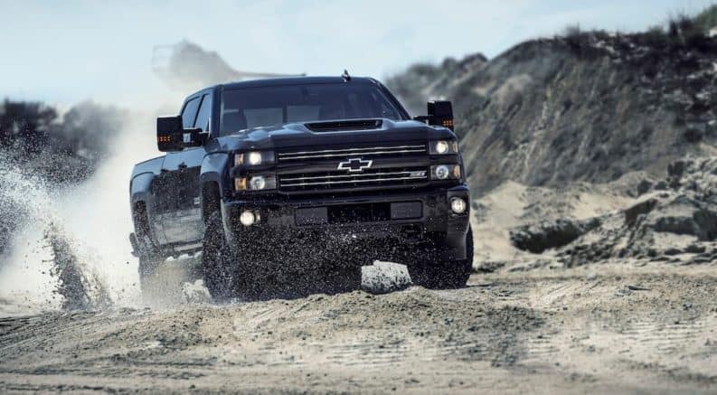 A black 2017 used Chevy Silverado 2500HD is driving on a dirt road with rock hills in the distance.