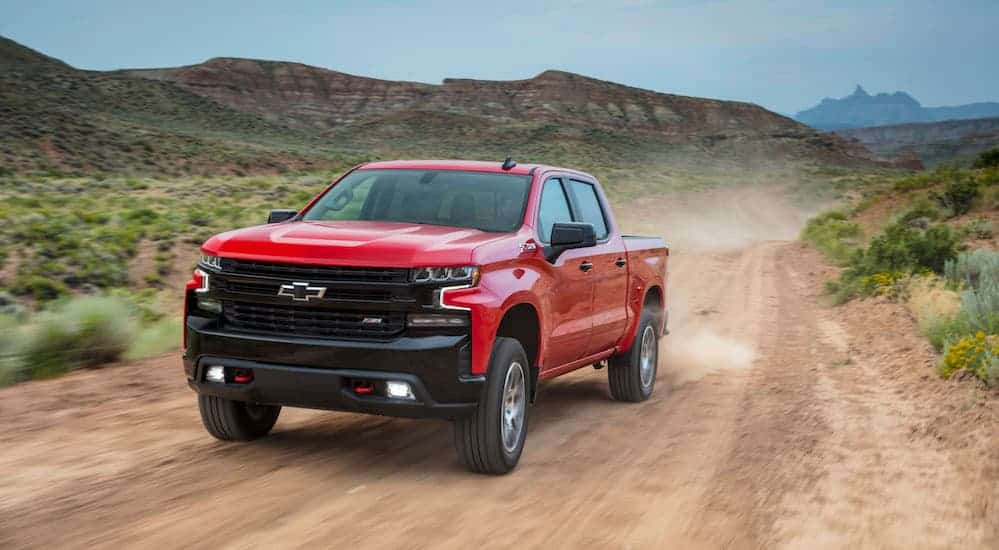 A red 2019 Chevy Silverado Trailboss is driving on a dirt road in the desert. 