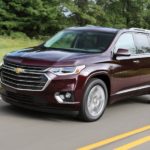 A burgundy 2018 Chevy Traverse, popular among used SUVs, is driving on a tree-lined road.