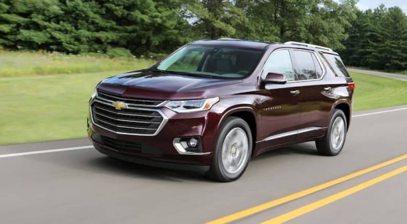 A burgundy 2018 Chevy Traverse, popular among used SUVs, is driving on a tree-lined road.